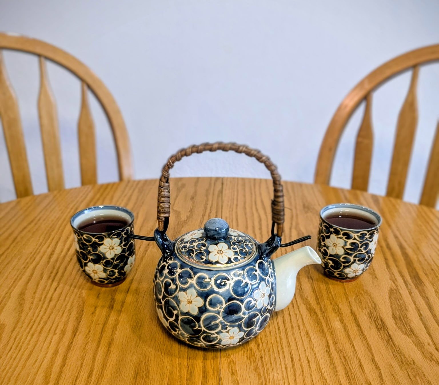 This is a photograph of two full teacups with a kettle resting on a table with two empty chairs. Its purpose is to communicate the sense of casual, inviting, and connected nature present in a somatic coaching session. Copyright 2026 by Stephen Peterson, photographer
